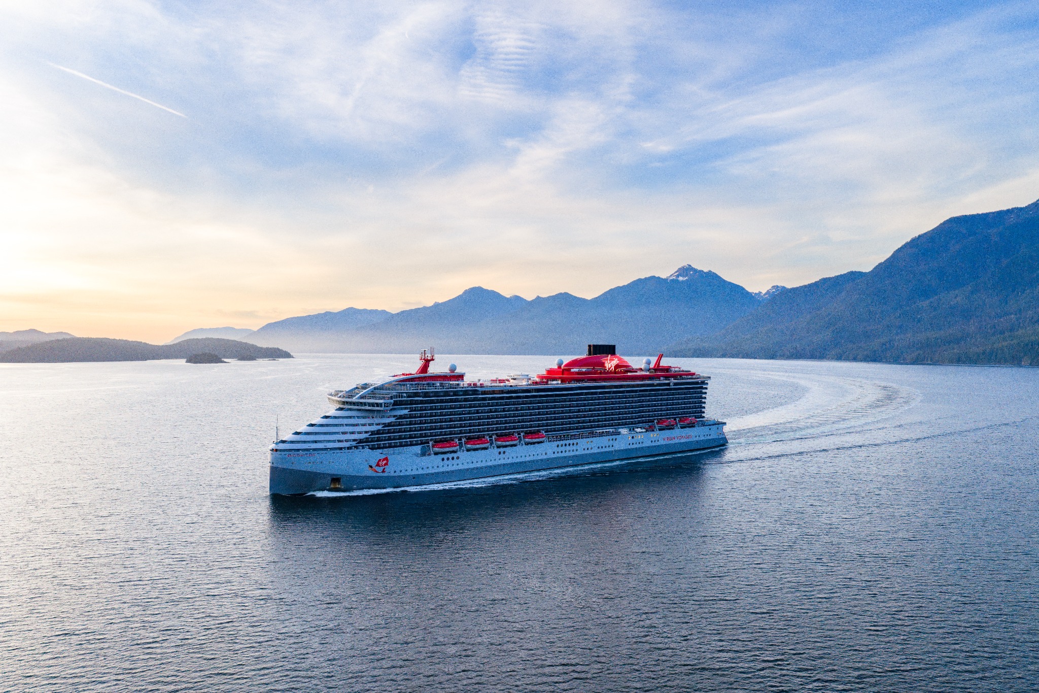A Virgin Voyages ship sailing past forested coastlines